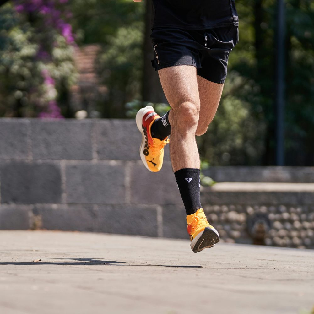 Person running outdoors with focus on legs wearing black shorts and orange running shoes.