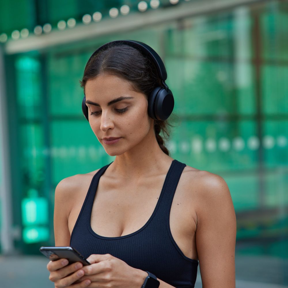 Woman wearing headphones and using a phone in an urban setting