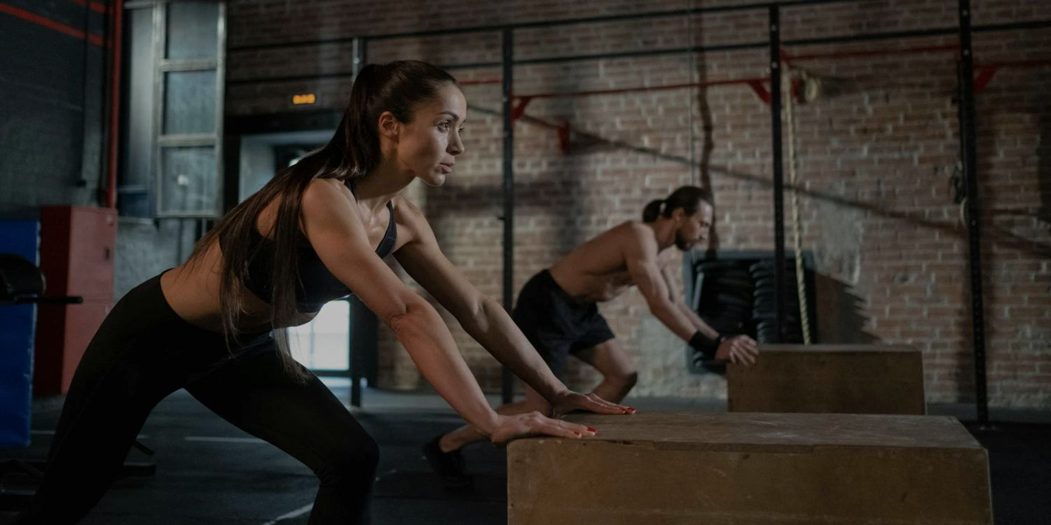 Two people performing box jumps in a gym setting.